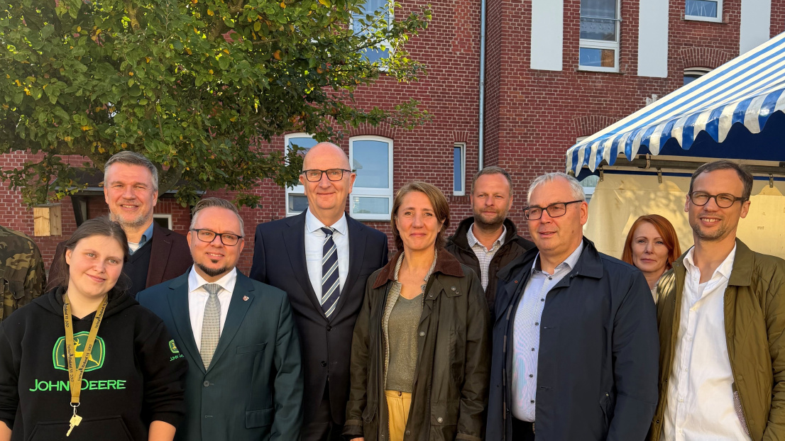 eine Gruppe von Menschen steht vor einem roten Backsteingebäude zu einem Gruppenfoto zusammen