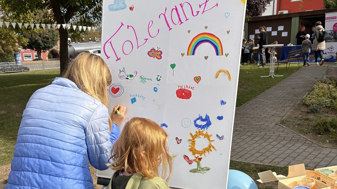 Eine Frau und ein kleines Mädchen malen auf einer Maltafel ein Bild mit dem Wort Toleranz.