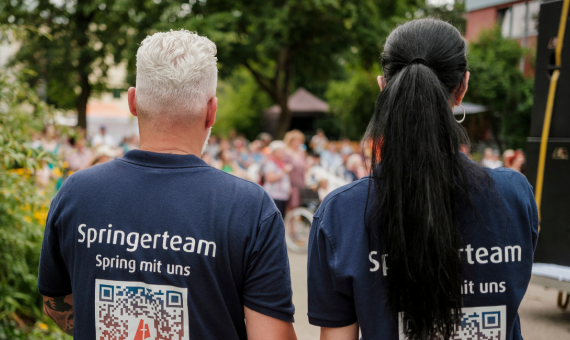 Ein Mann und eine Frau stehe mit den Rücken zur Kamera. Auf den T-Shirts steht Springerteam.