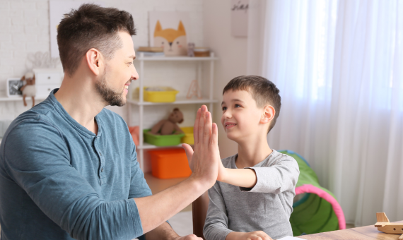 Ein Junge und ein junger Mann sitzen gegenüber, schauen sich an und machen einen Handschlag dabei.