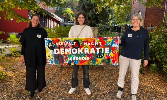 Drei Frauen stehen und halten zusammen ein selbstgemachtes Schild mit Schriftzug Demokratie