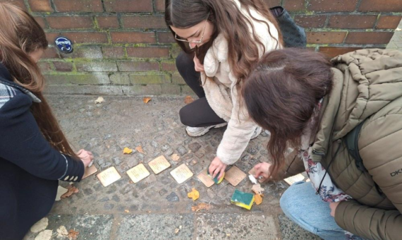 Drei junge Mädchen machen die Stolpersteine auf dem Pflasterweg sauber.