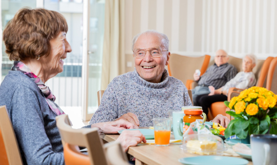En älterer Herr sitzt mit anderen Seniorinnen am Frühstückstisch.