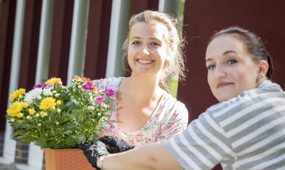 Zwei junge Frauen pflanzen Blumen in einen Blumentopf