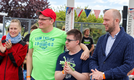 Drei Männer und eine Frau stehen zusammen und schauen fröhlich.
