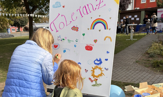 Eine Frau und ein kleines Mädchen malen auf einer Maltafel ein Bild mit dem Wort Toleranz.